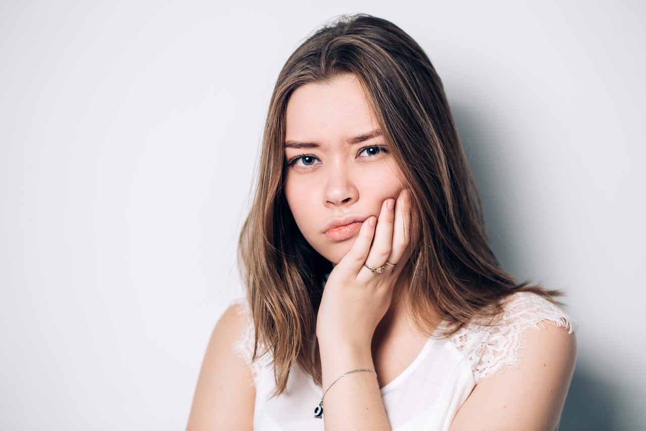 wisdom tooth extraction - Lady holding cheek in pain as she's having a tooth ache