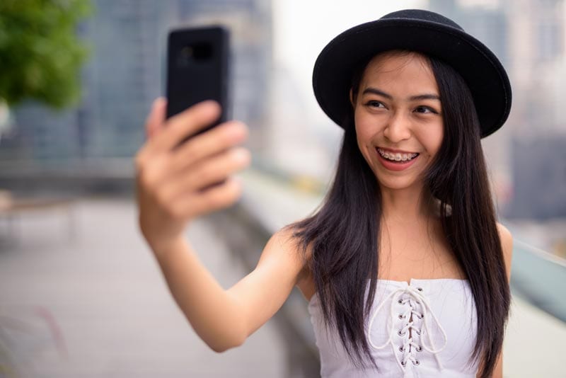 Braces lady holding phone to her face taking selfie | Braces treatment in singapore