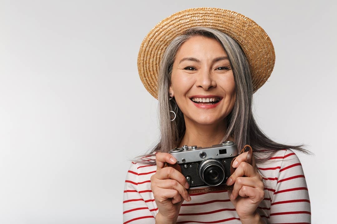 dental implant procedure in singapore - lady wearing sun hat and holding camera happy with her brand new dental implants in Singapore
