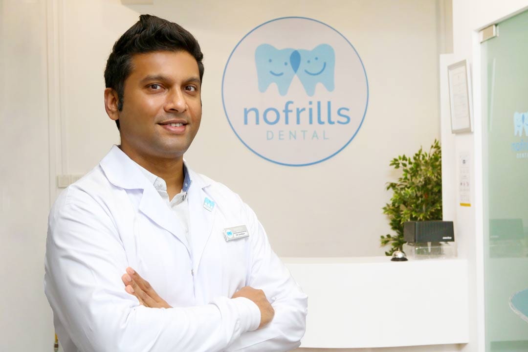 dentist standing in front of signage of nofrills dental