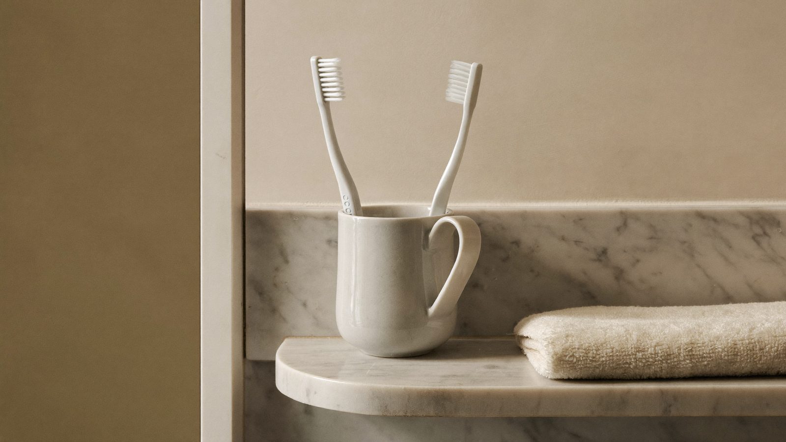 Two toothbrushes in a ceramic cup on a bathroom shelf, the basis of a daily oral hygiene routine