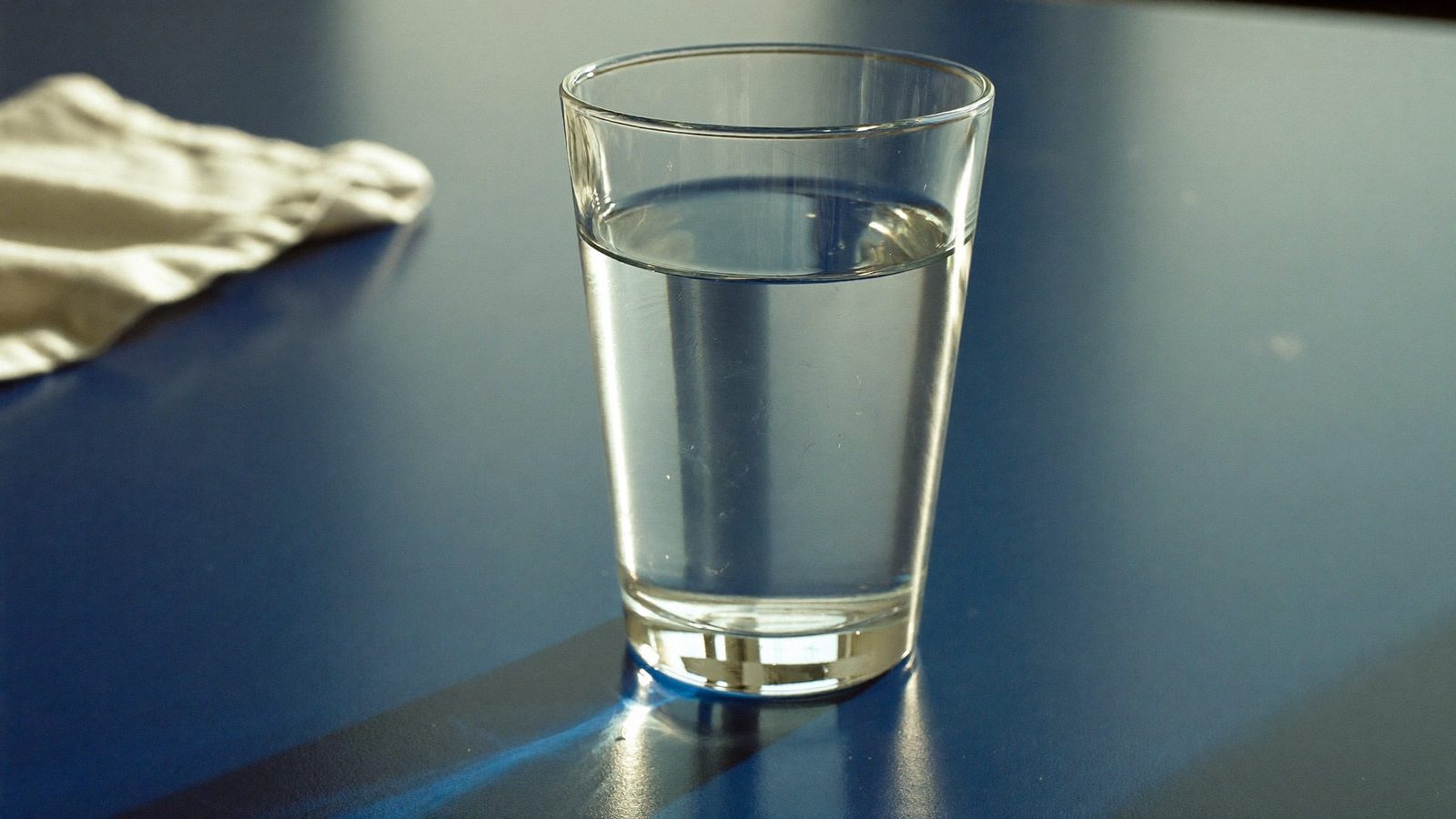 A plain glass of water beside a folded white cloth, for storing a denture overnight