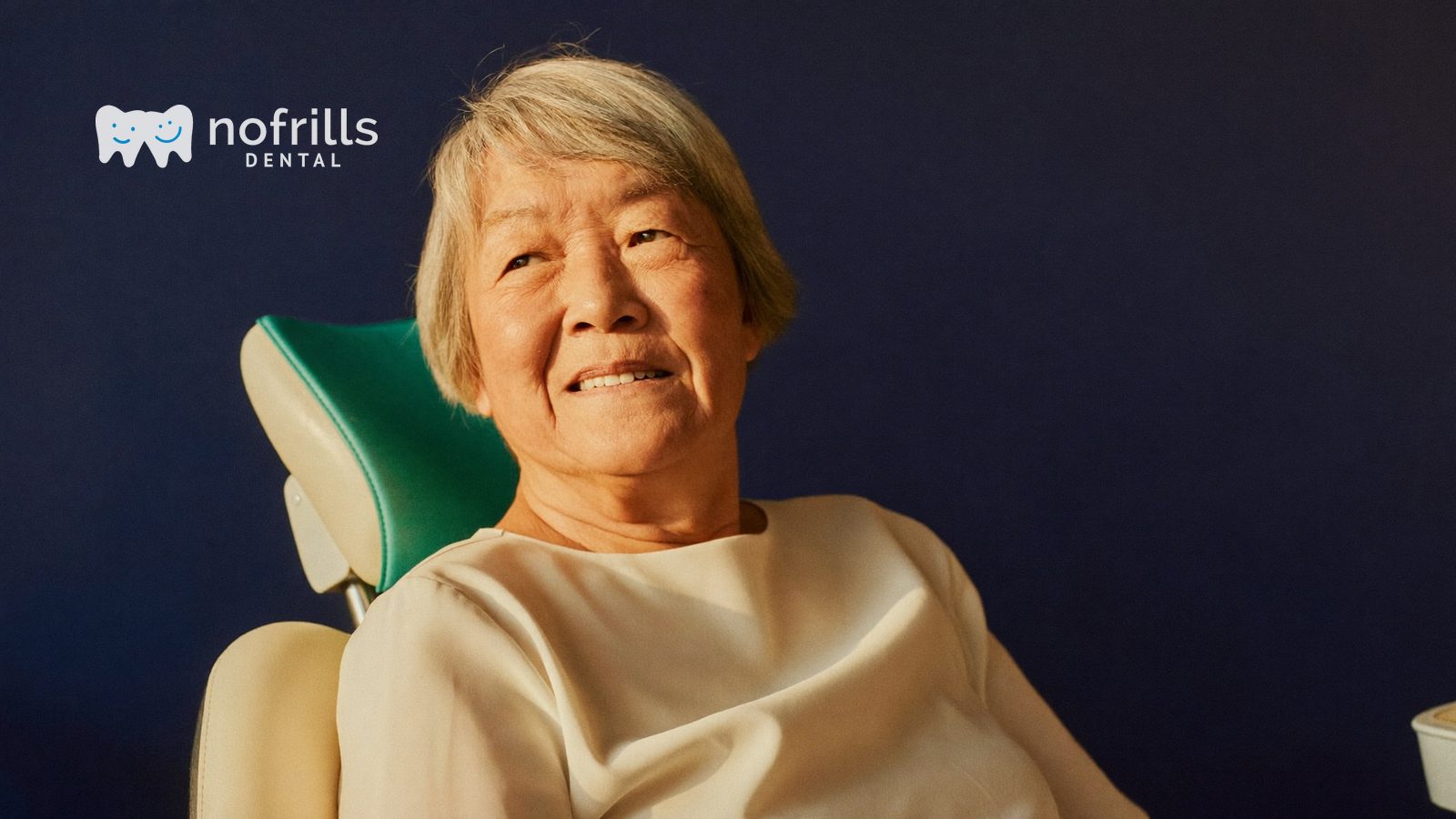 An older Singaporean woman smiling while seated in a dental chair at a NoFrills Dental clinic in Singapore