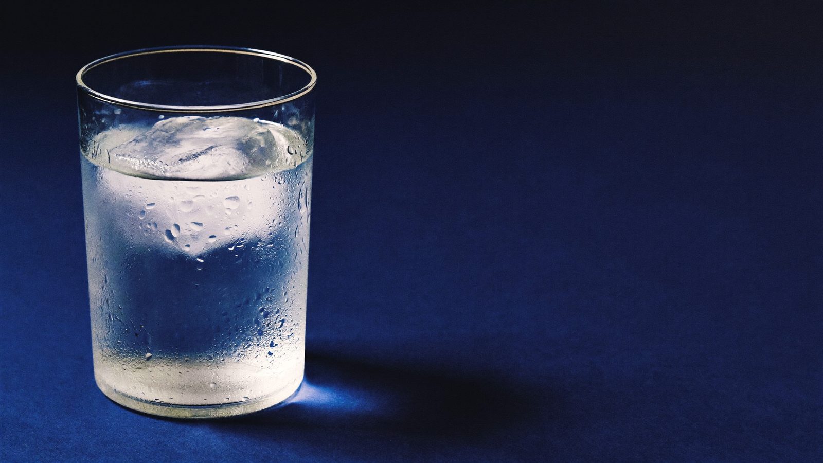Glass of iced water with condensation on a deep navy surface
