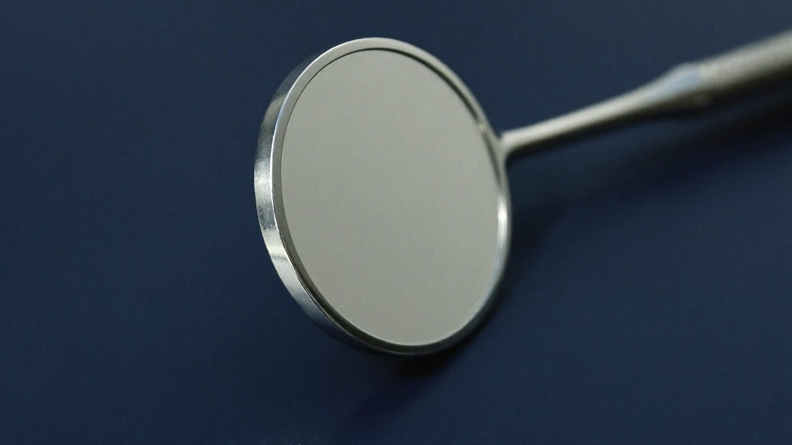 Dental mouth mirror resting on a deep navy surface