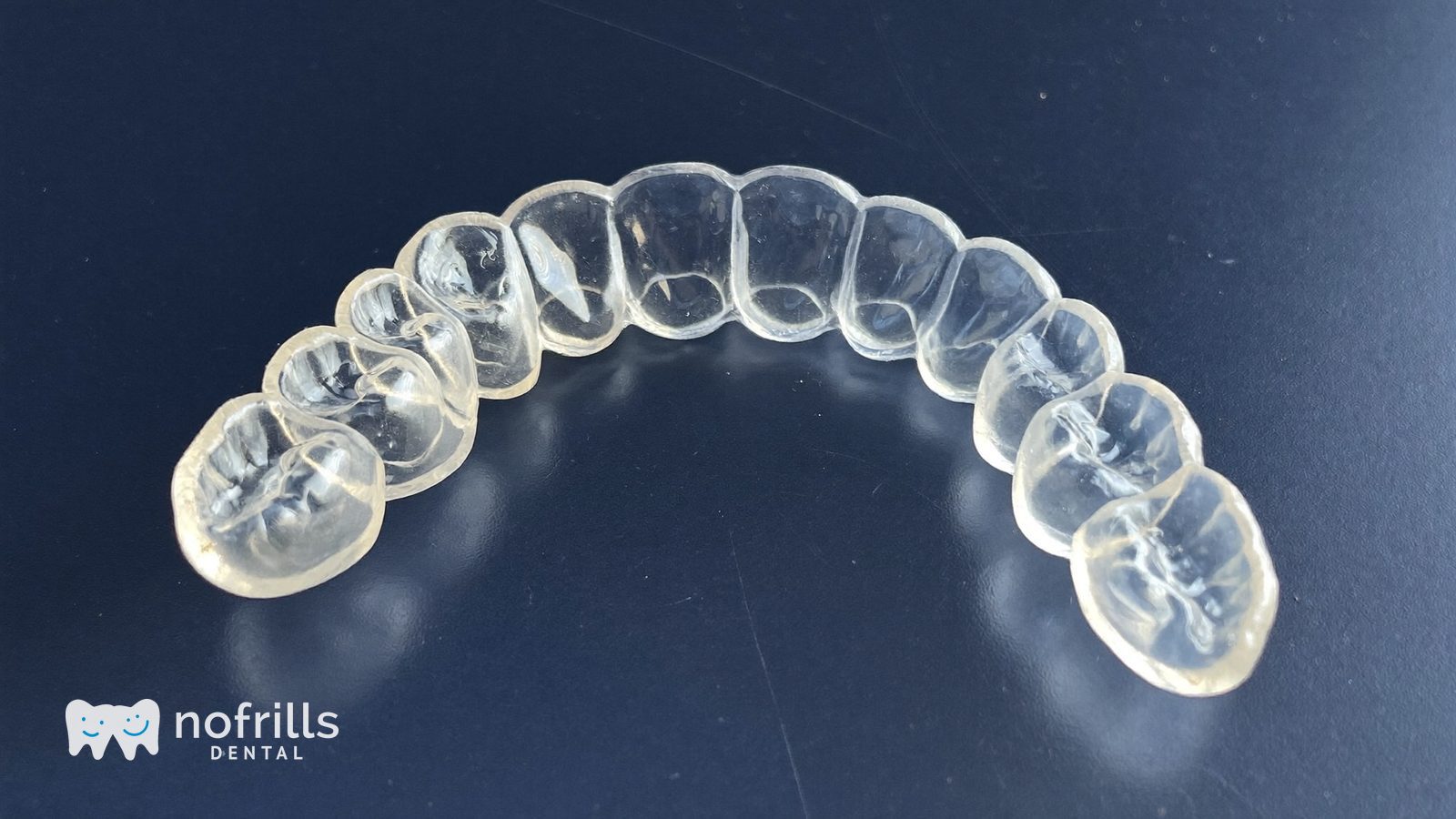 A clear custom made night guard photographed on a deep navy surface at a NoFrills Dental clinic in Singapore